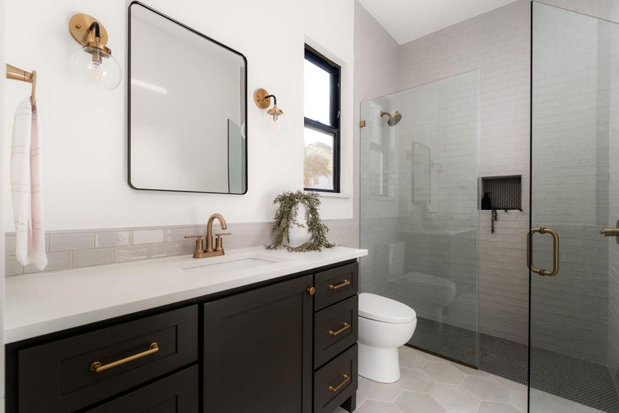 A well-lit bathroom features a spacious shower and elegant vanity with modern fixtures.