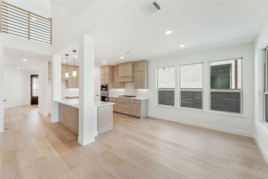 Open-concept living area and kitchen with light wood floors, tan cabinets, white countertops, and high ceilings Open-concept living area and kitchen with light wood floors, tan cabinets, white countertops, and high ceilings