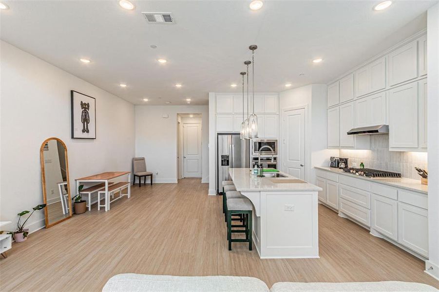 Kitchen with a breakfast bar, white cabinets, an island with sink, recessed lighting, and light wood finished floors