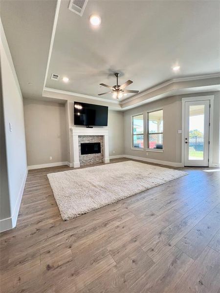 Unfurnished family room open to kitchen area with comfy fire place light hardwood / wood-style floors, a raised ceiling, ceiling fan, and crown molding