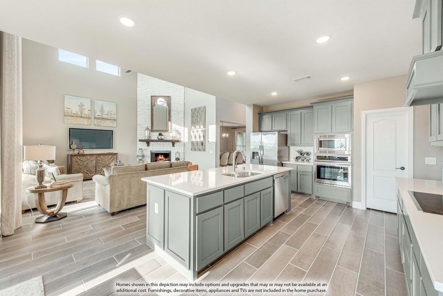 Open-concept kitchen with gray cabinets, large island, and stainless appliances, open to living room with fireplace