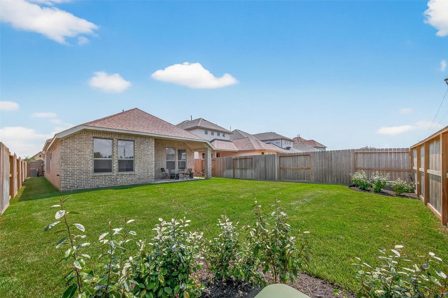 This photo showcases a spacious backyard with a neatly maintained lawn, bordered by a wooden fence. The brick house features a cozy covered patio, ideal for outdoor seating and relaxation. This photo showcases a spacious backyard with a neatly maintained lawn, bordered by a wooden fence. The brick house features a cozy covered patio, ideal for outdoor seating and relaxation.