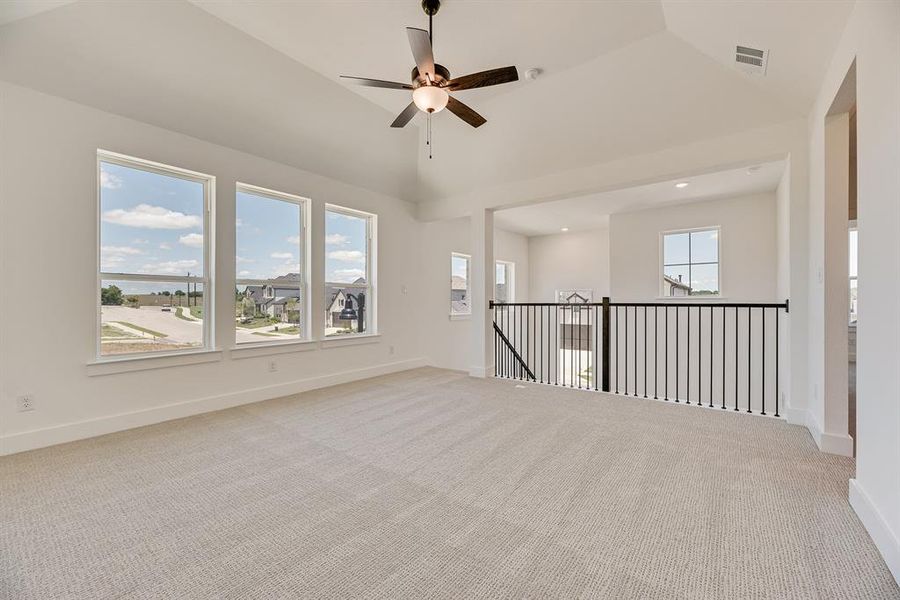 Empty room with light carpet, lofted ceiling, and ceiling fan Empty room with light carpet, lofted ceiling, and ceiling fan