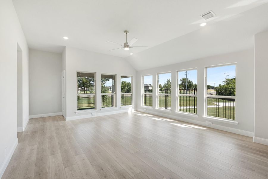Open living room with vaulted ceiling, ceiling fan, light wood floors, and large windows overlooking a backyard