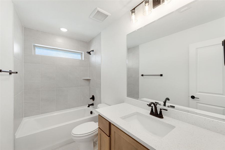 Full bathroom with tiled tub-shower combo, single vanity with white countertop, and large mirror