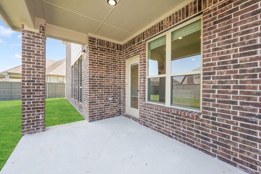 Covered back patio with concrete floor, brick columns, and fenced backyard with green lawn