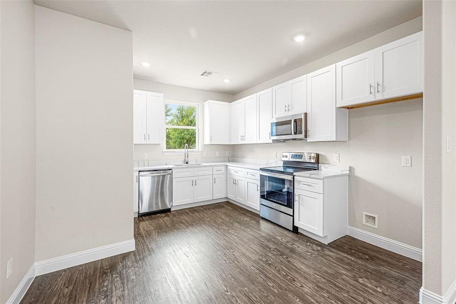 Kitchen with stainless steel appliances, dark wood-type flooring, sink, and white cabinetry