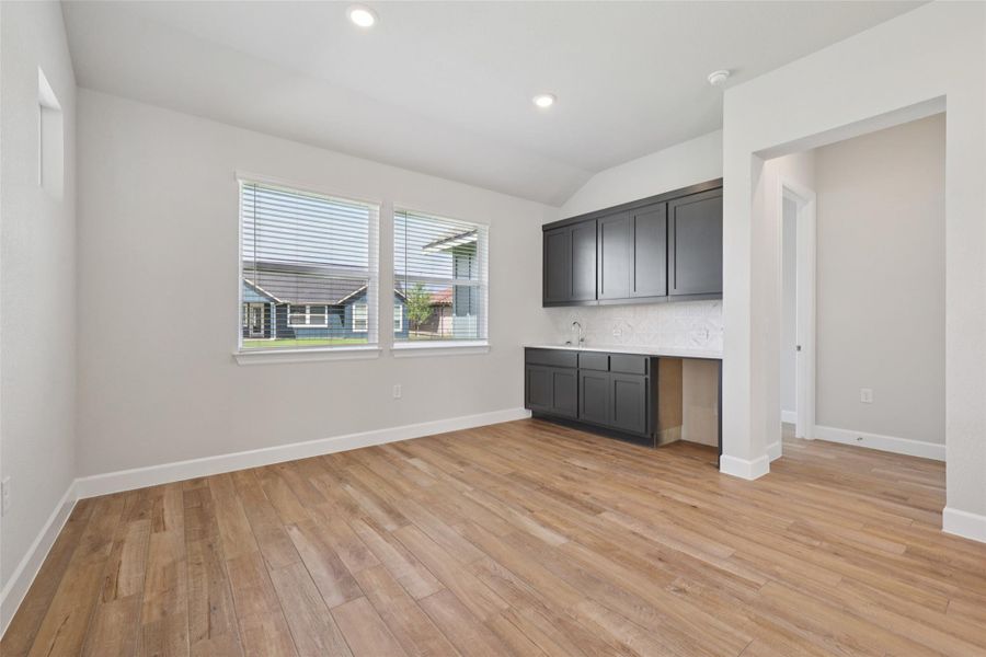 Indoor wet bar with light wood-style flooring, backsplash, lofted ceiling, and recessed lighting
