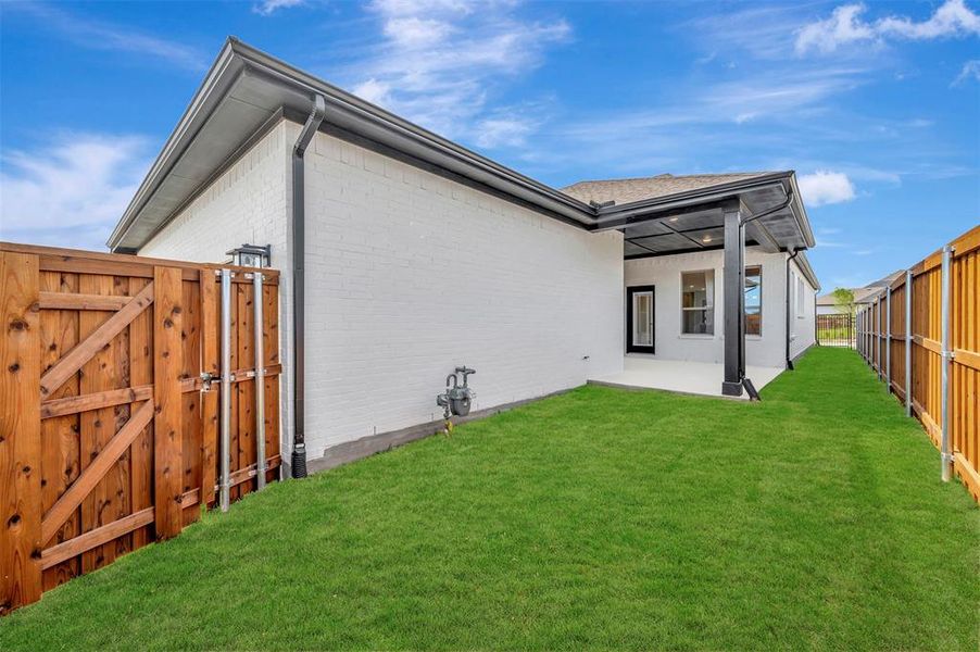 Rear view of house featuring a fenced backyard, brick siding, a gate, and a patio area