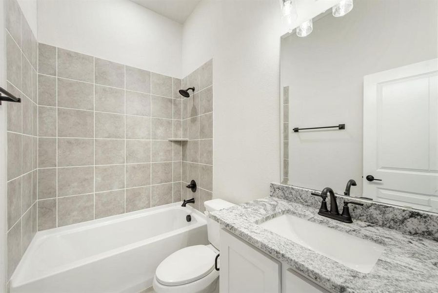 Bathroom featuring a built-in tub with tile surround, a vanity with a white countertop and integrated sink, and matte black fixtures Bathroom featuring a built-in tub with tile surround, a vanity with a white countertop and integrated sink, and matte black fixtures