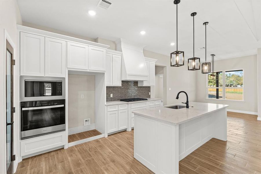 Kitchen with stainless steel oven, tasteful backsplash, white cabinets, decorative light fixtures, and light wood-style flooring