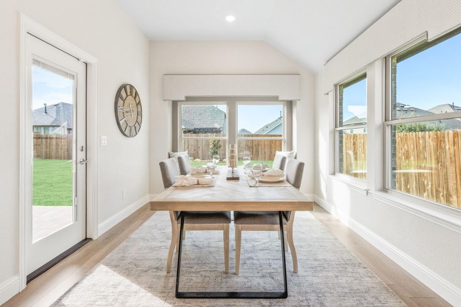 Bright dining room with wood table, gray chairs, vaulted ceiling, and glass door to backyard Bright dining room with wood table, gray chairs, vaulted ceiling, and glass door to backyard