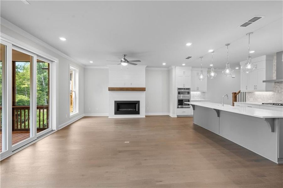 Kitchen featuring ornamental molding, white cabinetry, wall chimney range hood, dark wood-type flooring, and a center island with sink Kitchen featuring ornamental molding, white cabinetry, wall chimney range hood, dark wood-type flooring, and a center island with sink