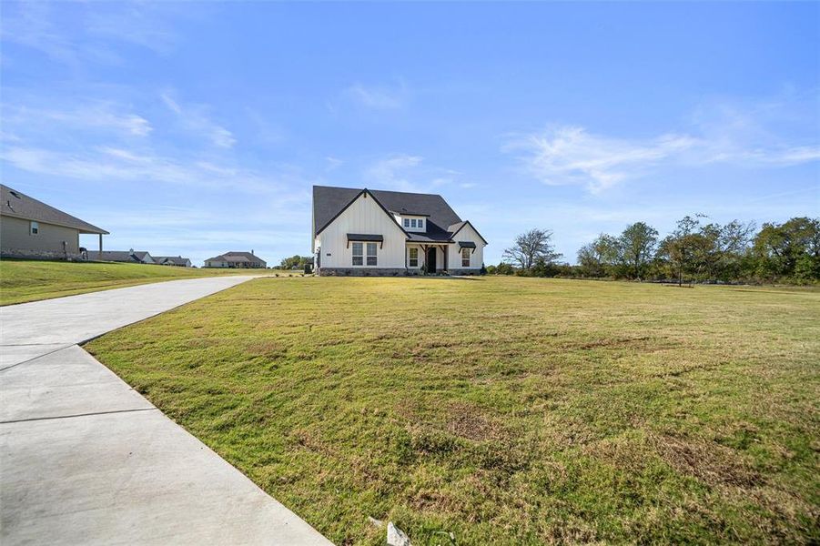 Modern inspired farmhouse with a front yard, concrete driveway, and board and batten siding
