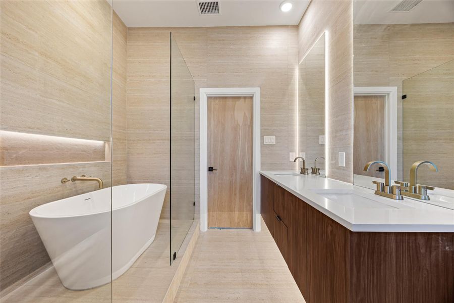 Full bath featuring double vanity, a freestanding tub, tiled shower, tile walls, and light tile patterned floors
