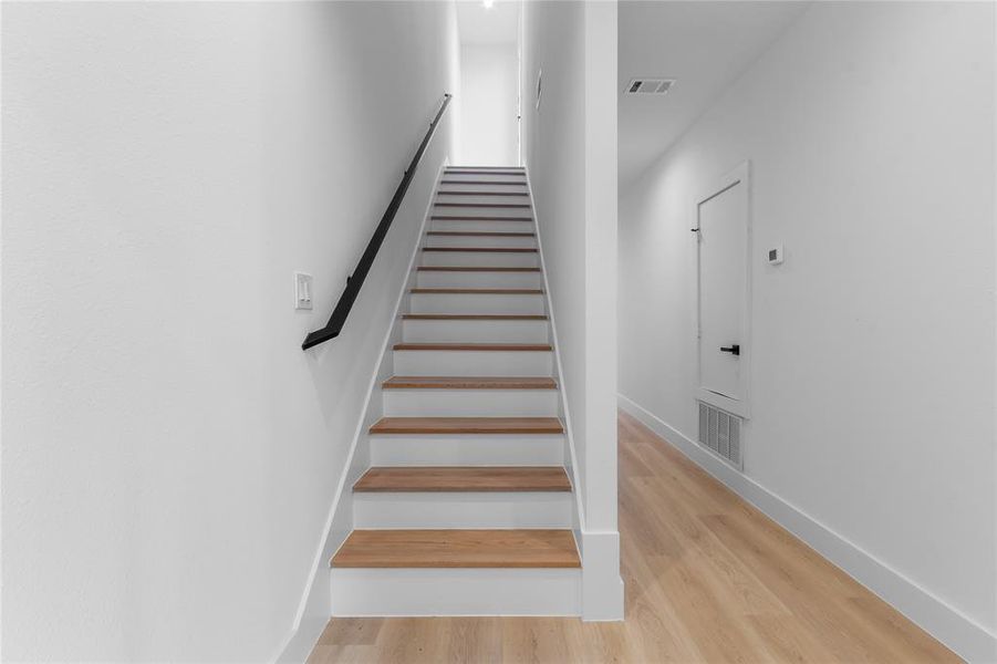 Staircase featuring wood-finish treads and white risers with a black wall-mounted handrail Staircase featuring wood-finish treads and white risers with a black wall-mounted handrail