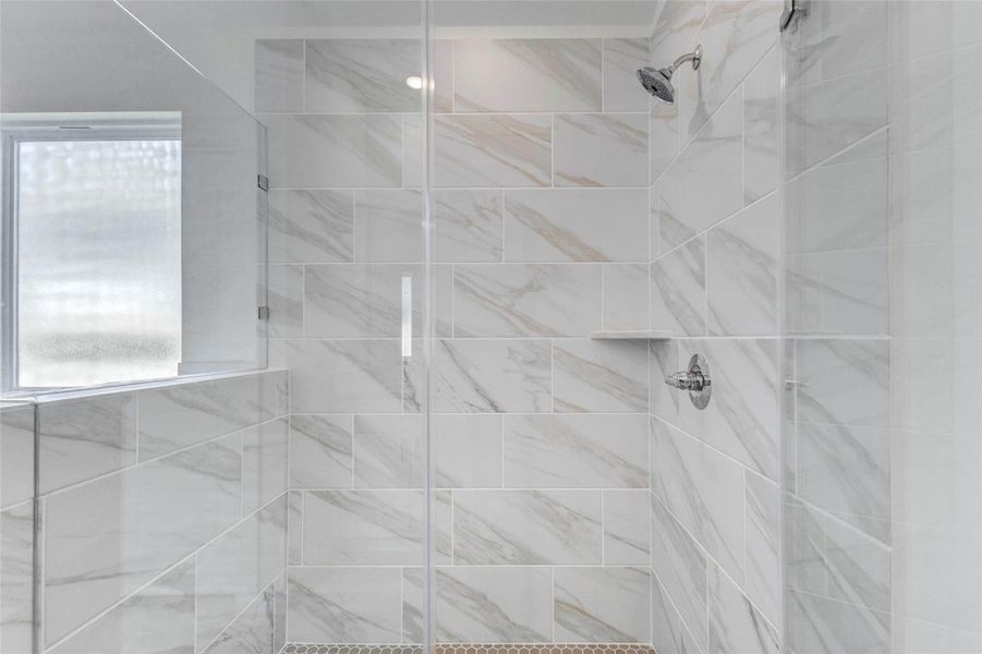 Separate primary shower with a glass enclosure, chrome fixtures, built-in ledge, and marble-look tile extending across the walls. The clean design gives the bathroom a modern, spa-inspired feel while providing a bright and polished shower space.
