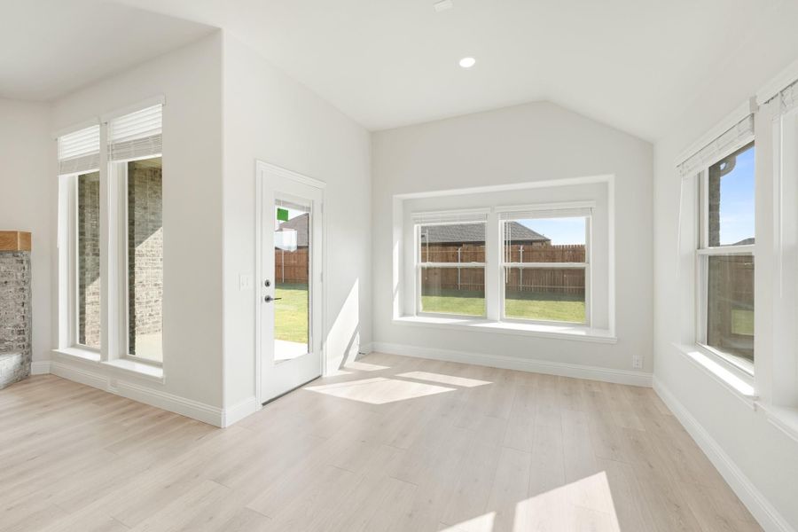 Bright empty living room with vaulted ceiling, light wood floors, and large windows overlooking backyard