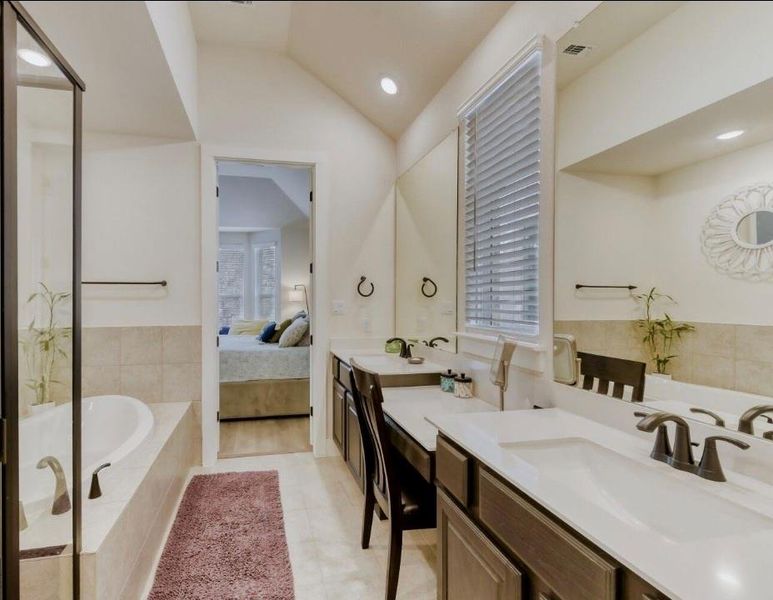 Ensuite bathroom featuring a bath, lofted ceiling, two vanities, light tile patterned floors, and recessed lighting