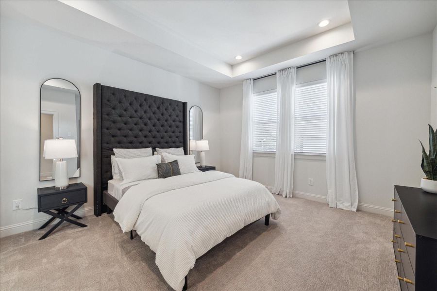 This spacious primary bedroom offers a serene retreat with soft carpeting and large windows that flood the room with natural light. The recessed ceiling and neutral color palette create a soothing and airy ambiance, perfect for relaxation.