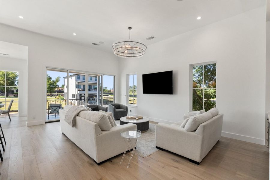 A spacious, naturally illuminated living room featuring hardwood floors and a contemporary chandelier. A spacious, naturally illuminated living room featuring hardwood floors and a contemporary chandelier.