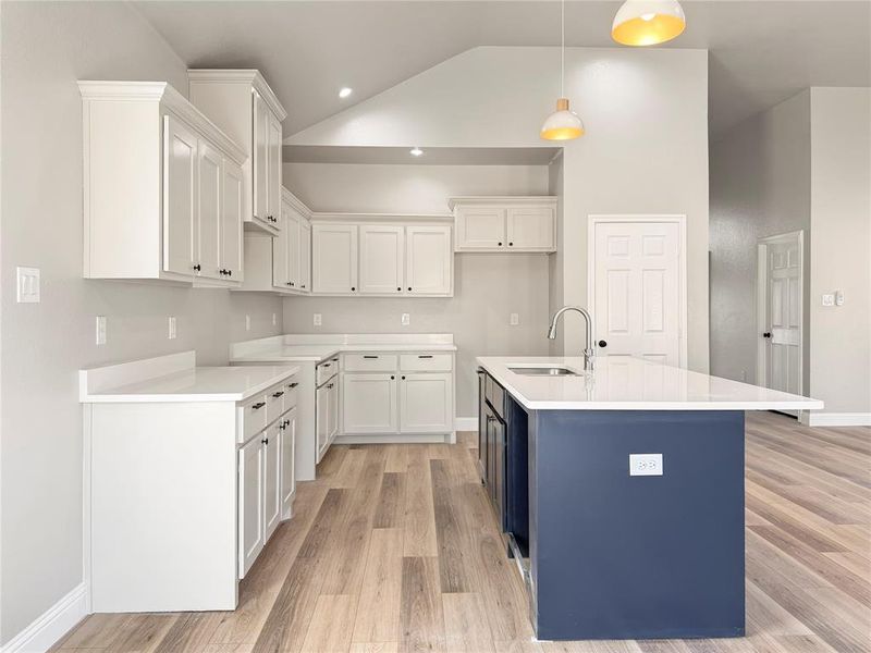 Dual tone kitchen with dual tone cabinetry, light wood finished floors, a kitchen island with sink, light stone counters, and lofted ceiling Dual tone kitchen with dual tone cabinetry, light wood finished floors, a kitchen island with sink, light stone counters, and lofted ceiling