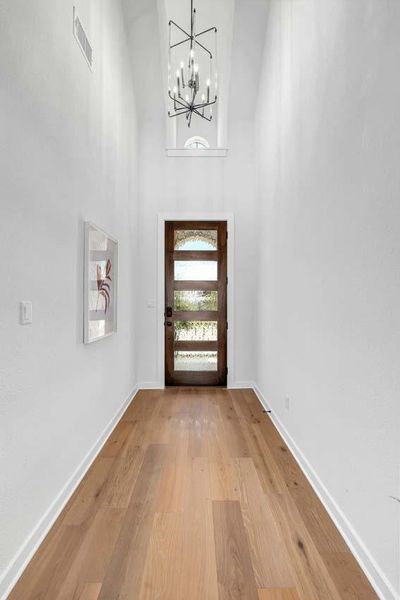 Entryway featuring an inviting chandelier, wood finished floors, baseboards, and visible vents