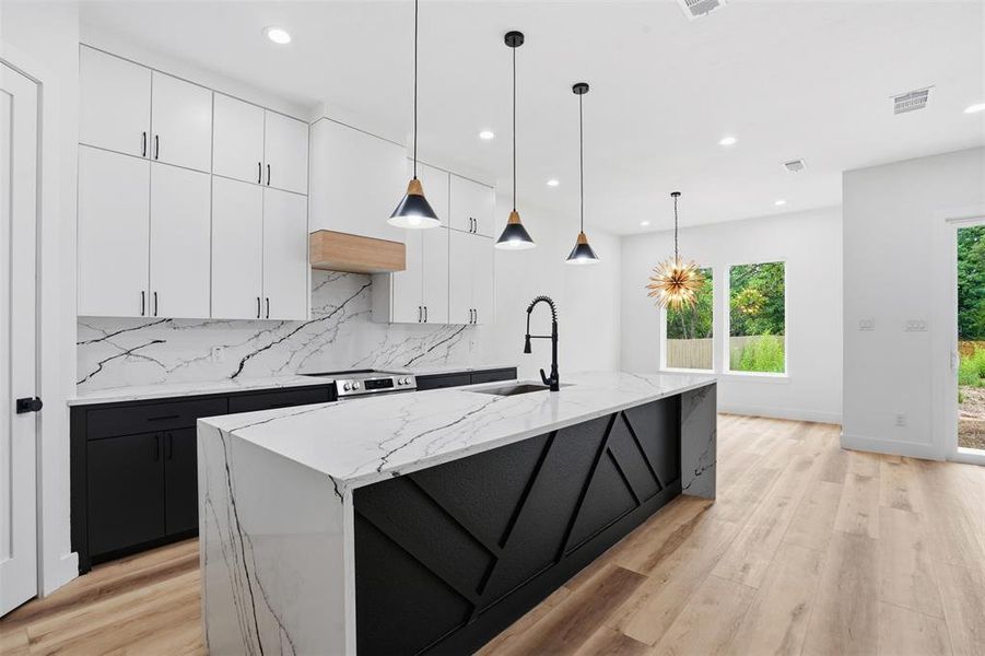 Kitchen featuring a waterfall island with black paneled base, white countertops with prominent veining, and a matte black faucet