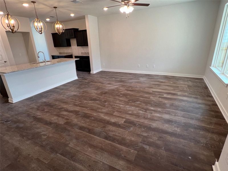 Kitchen with hanging light fixtures, dark cabinets, light stone counters, a center island with sink, and dark wood-style floors Kitchen with hanging light fixtures, dark cabinets, light stone counters, a center island with sink, and dark wood-style floors