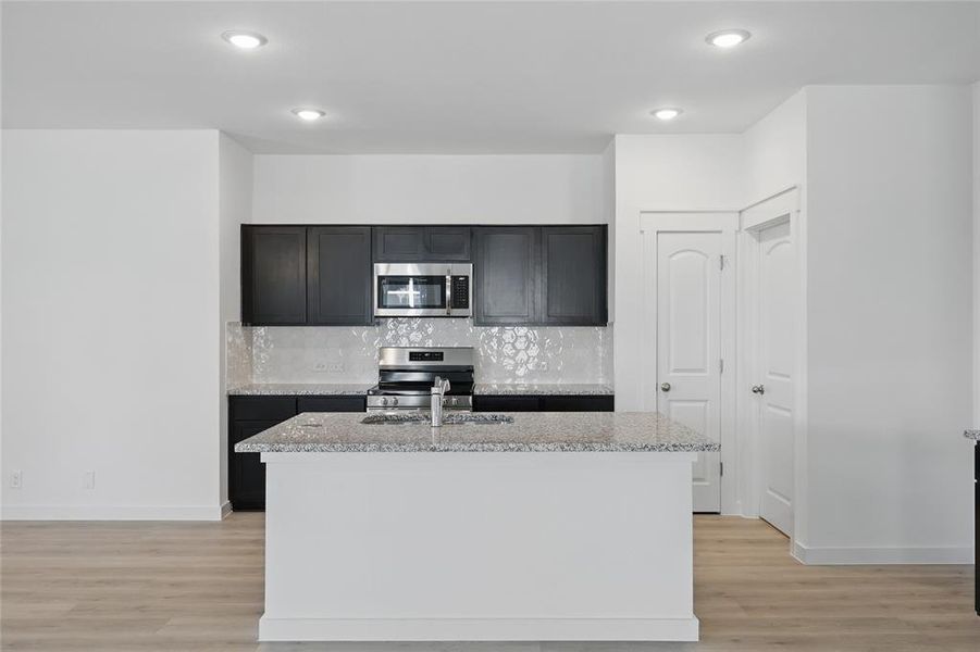 Kitchen with light wood-style flooring, appliances with stainless steel finishes, a sink, and backsplash Kitchen with light wood-style flooring, appliances with stainless steel finishes, a sink, and backsplash