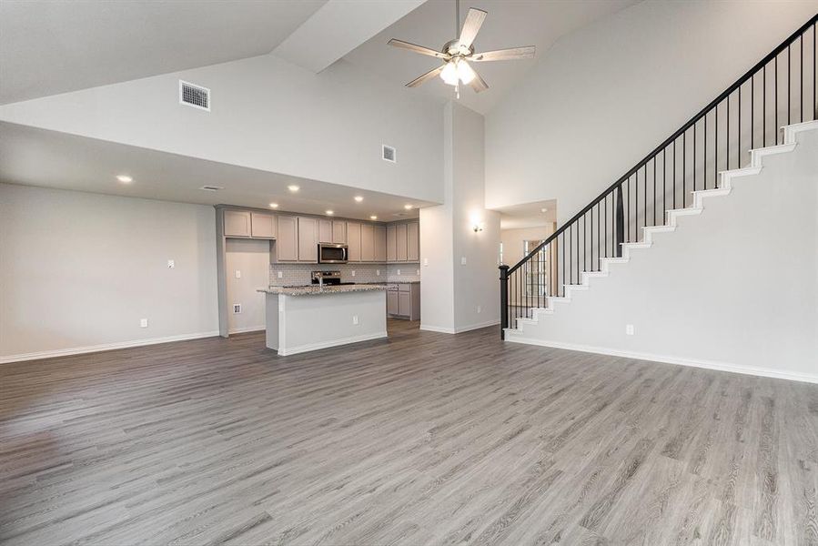 Unfurnished living room with ceiling fan, high vaulted ceiling, and light hardwood / wood-style flooring