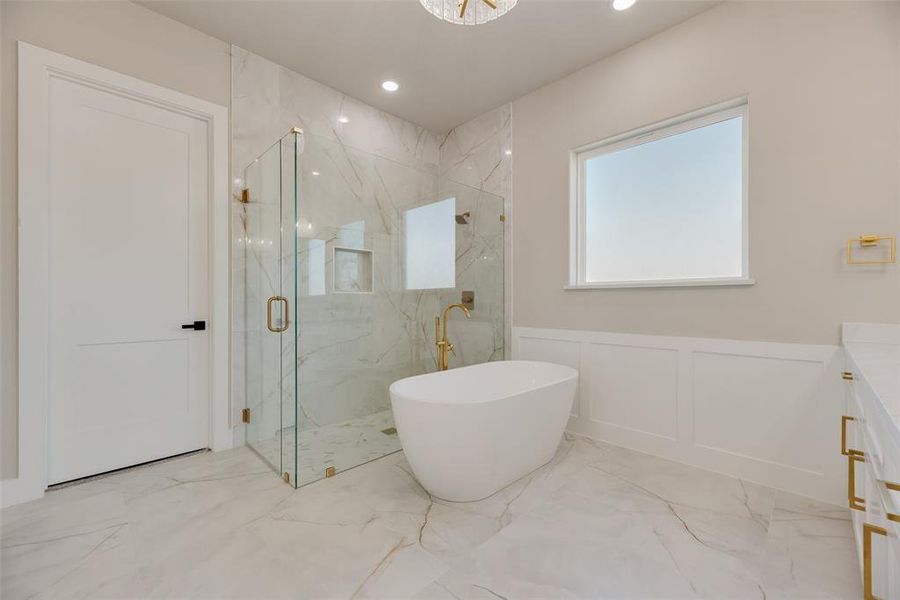 Bathroom with light marble finish floors, a marble finish shower, wainscoting, a soaking tub, and vanity