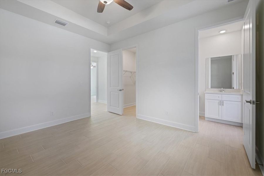 Unfurnished bedroom featuring ensuite bath, a spacious closet, wood tiled floors, and a raised ceiling Unfurnished bedroom featuring ensuite bath, a spacious closet, wood tiled floors, and a raised ceiling