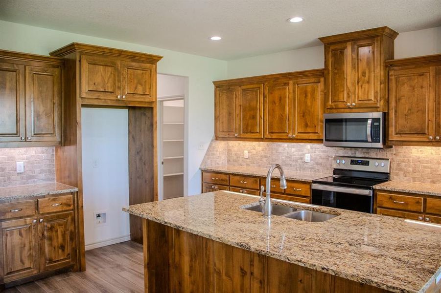 Kitchen with appliances with stainless steel finishes, backsplash, brown cabinetry, and recessed lighting Kitchen with appliances with stainless steel finishes, backsplash, brown cabinetry, and recessed lighting