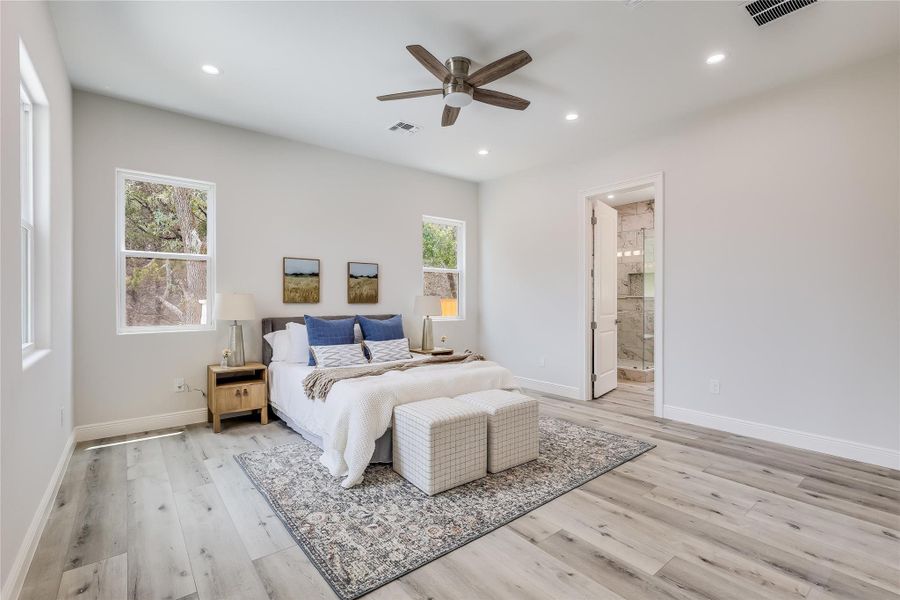 Bedroom with ceiling fan, multiple windows, connected bathroom, and light hardwood / wood-style floors