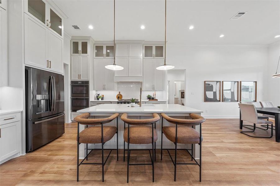 Kitchen featuring appliances with stainless steel finishes, light countertops, tasteful backsplash, a kitchen island with sink, and light wood-style flooring
