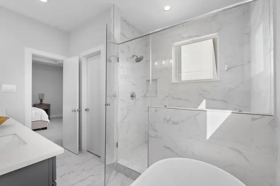 Luxurious spa-like bath with oversized walk-in shower, freestanding soaking tub, and full-height tile surround, delivering a sleek and modern aesthetic.
