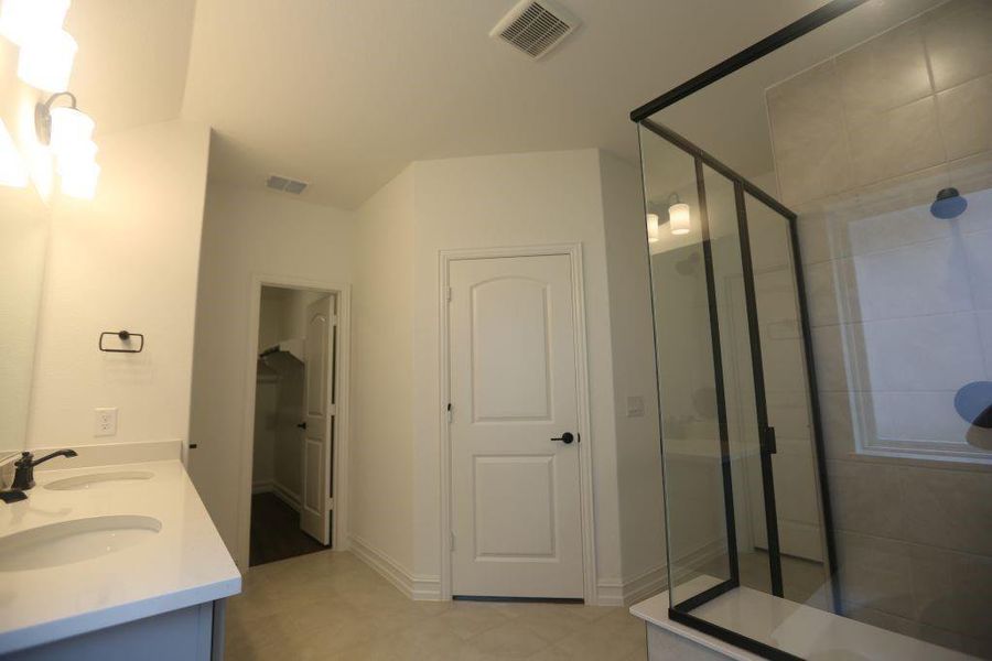 Contemporary bathroom featuring a dual vanity with undermount sinks, a framed glass shower enclosure, and neutral wall tile