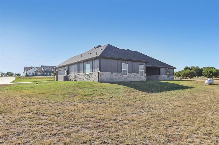 Rear view of property with board and batten siding, stone siding, and a lawn