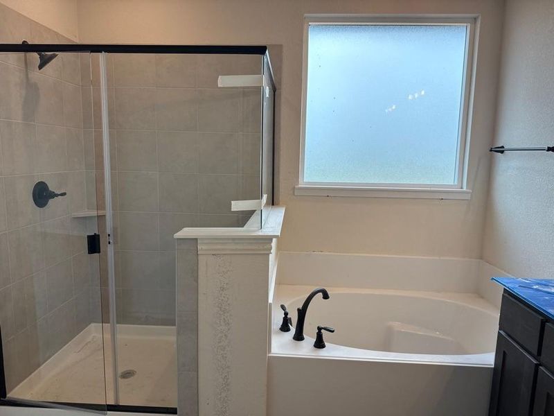 Bathroom featuring a built-in soaking tub with matte black fixtures, a tiled shower with a clear glass enclosure and matte black hardware, and a frosted window