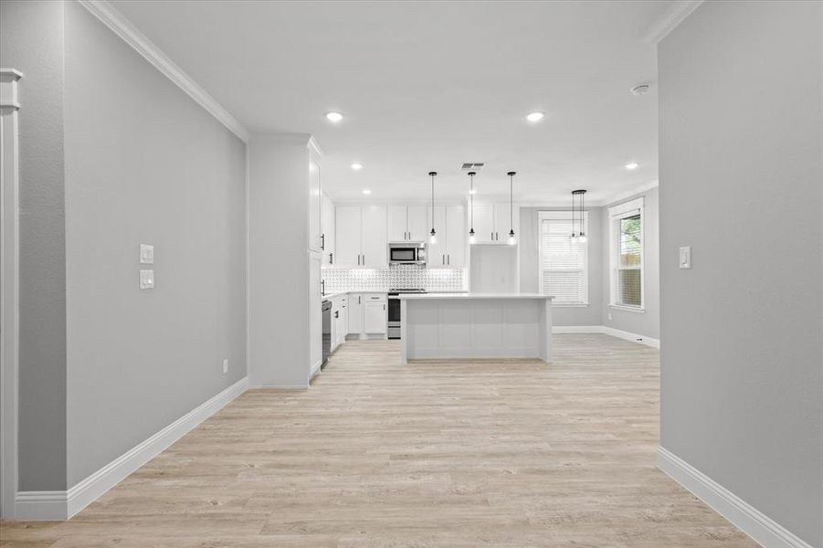 Kitchen featuring white cabinets, appliances with stainless steel finishes, light hardwood / wood-style floors, pendant lighting, and a kitchen island