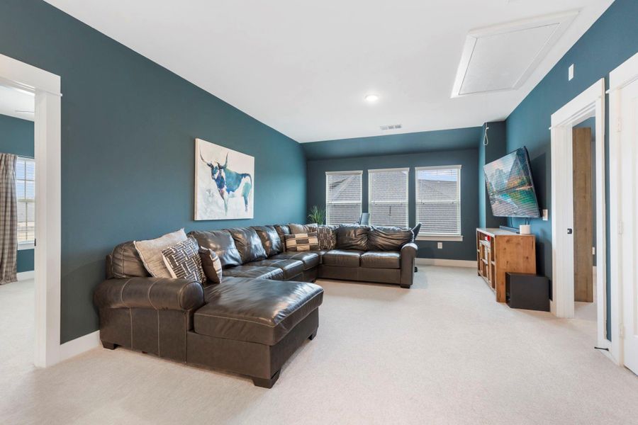 This cozy living room features dark teal walls, a large brown sectional sofa, and a mounted TV. Natural light streams in through multiple windows, enhancing the inviting atmosphere. Perfect for relaxation and entertainment.