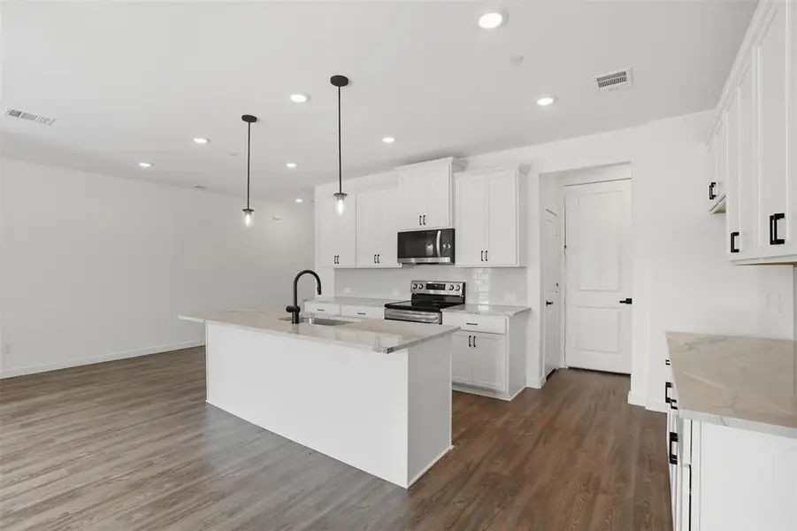 Kitchen with light stone countertops, a kitchen island with sink, white cabinets, decorative light fixtures, and stainless steel appliances Kitchen with light stone countertops, a kitchen island with sink, white cabinets, decorative light fixtures, and stainless steel appliances