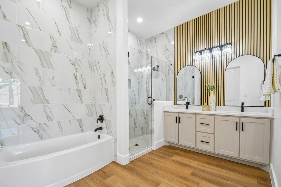 A spacious bathroom displays dual vanities, wood-look flooring, a glass-enclosed shower, and a soaking tub. A spacious bathroom displays dual vanities, wood-look flooring, a glass-enclosed shower, and a soaking tub.