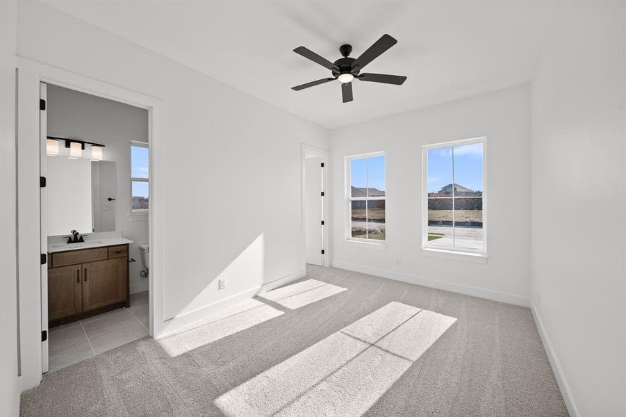 Unfurnished bedroom featuring light carpet, a ceiling fan, multiple windows, and ensuite bathroom