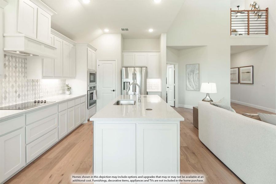 Open kitchen with white cabinets, large island with sink, stainless appliances, and light wood floors open to living area