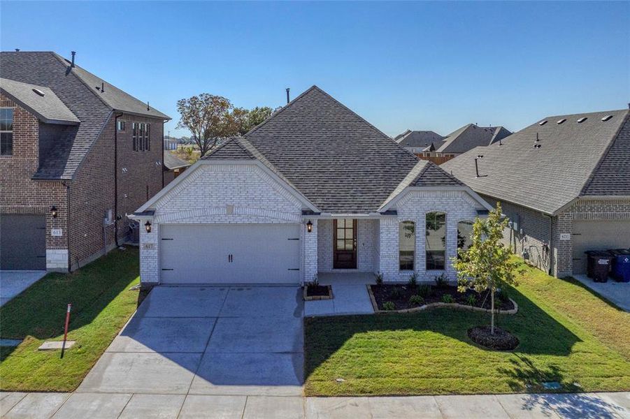 French country home with brick siding, a front lawn, driveway, an attached garage, and a shingled roof