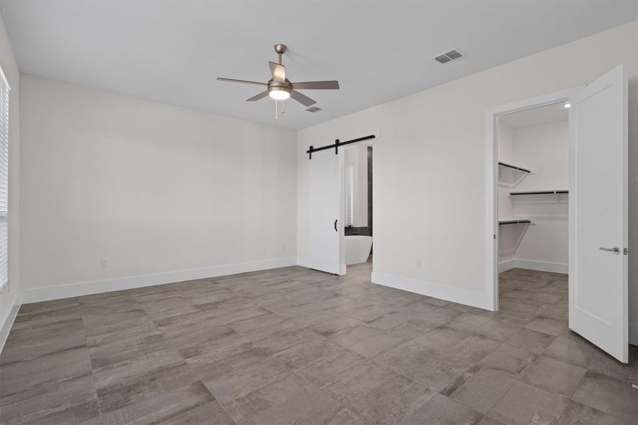 Unfurnished bedroom featuring a barn door, a spacious closet, and a ceiling fan Unfurnished bedroom featuring a barn door, a spacious closet, and a ceiling fan