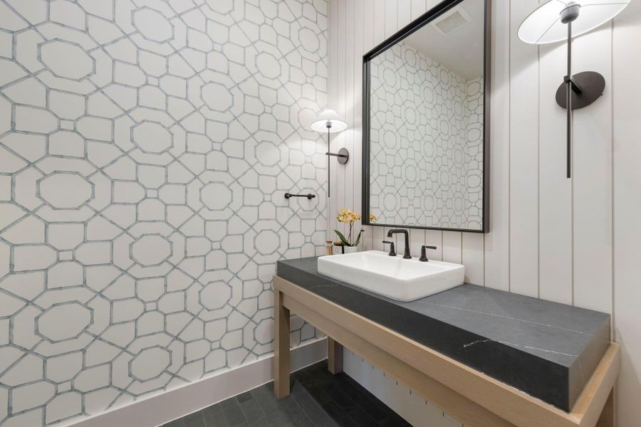 Designer powder bath featuring striking geometric wallpaper, a sleek stone vanity with vessel sink, and modern sconces that create a refined, contemporary feel.