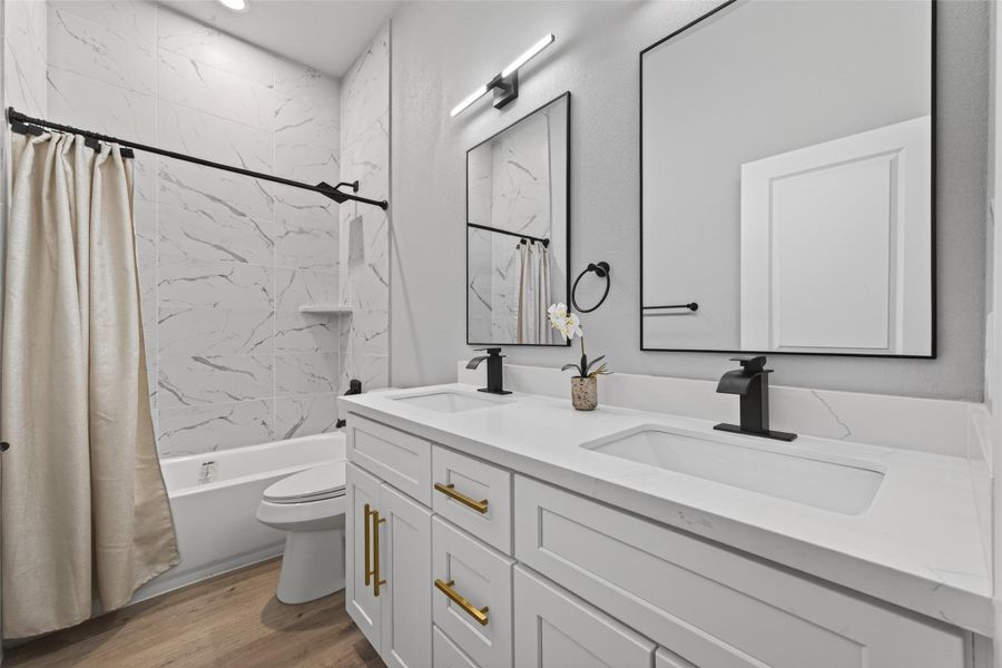 Spa-inspired secondary bathroom with dual-sink quartz vanity, custom cabinetry with brushed gold hardware, matte black fixtures, LED vanity lighting, and full-height marble-look tile surround.